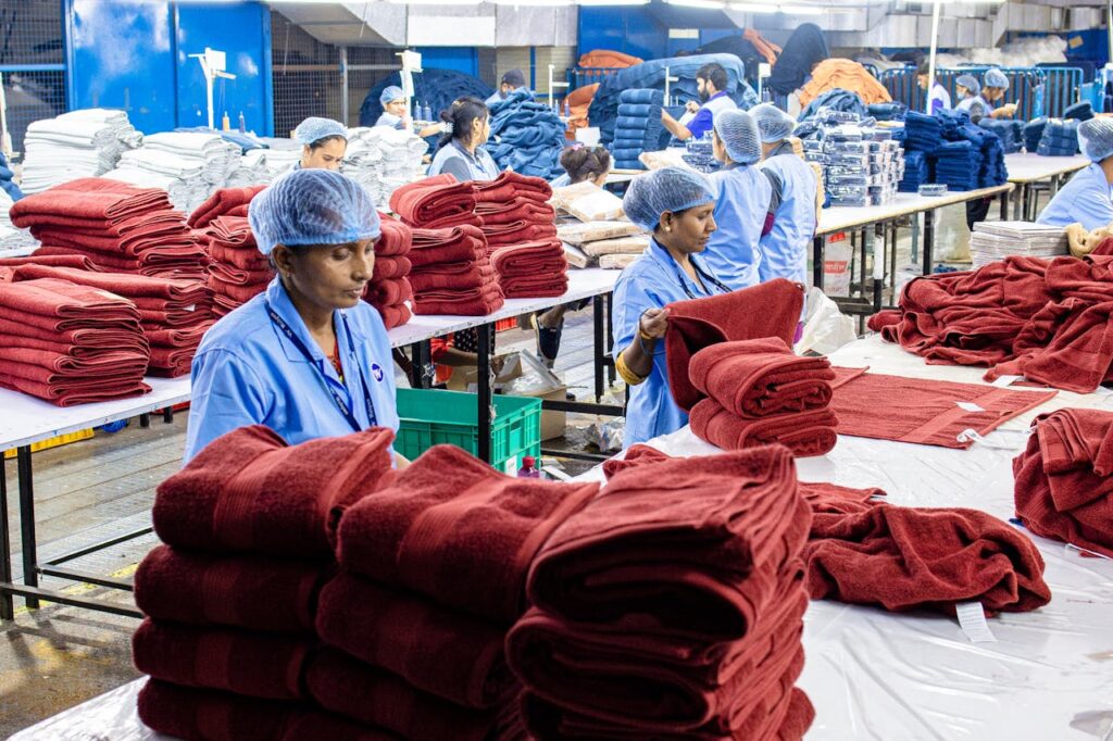 Workers in an Indian factory fold towels efficiently. Textile industry scene.