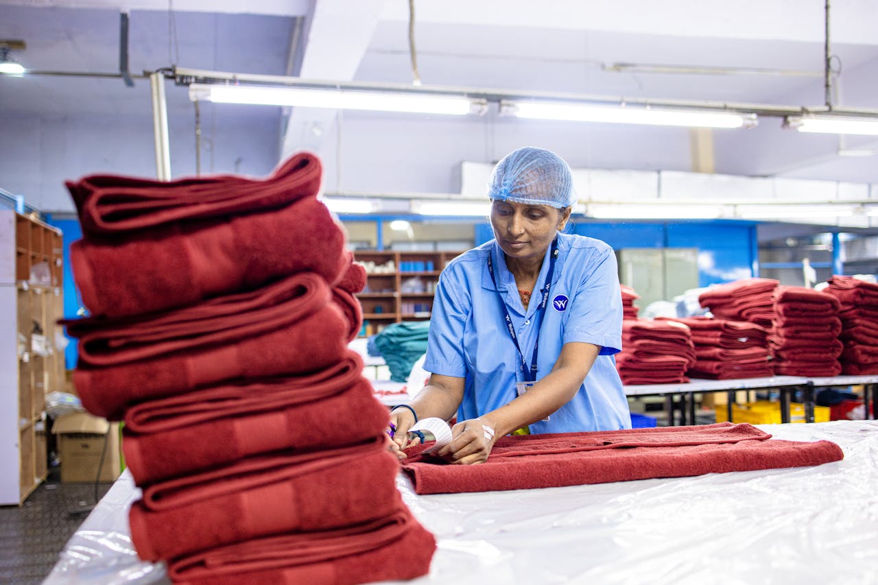 Female textile worker folding red towels in an industrial setting indoors.