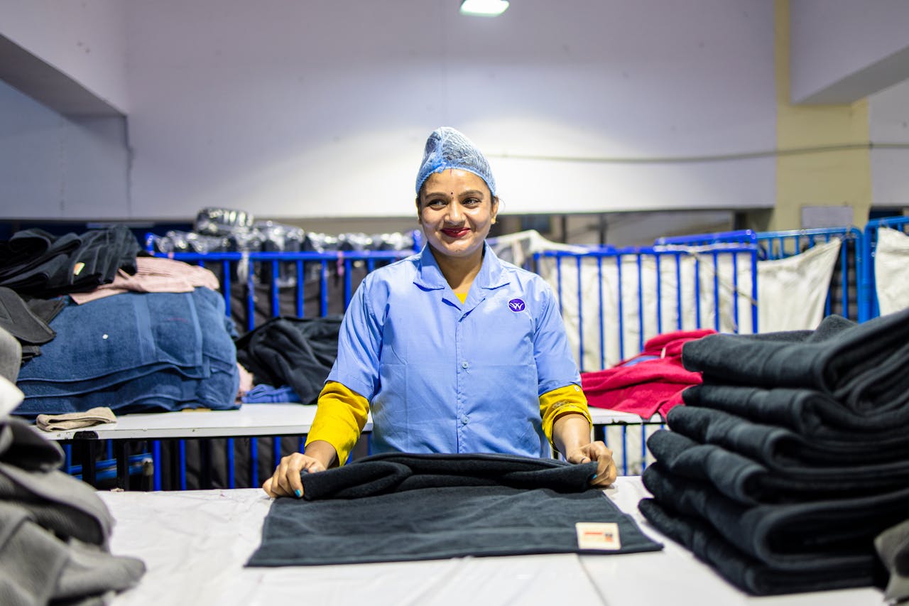 Female textile worker in uniform folding towels in a bright factory setting.